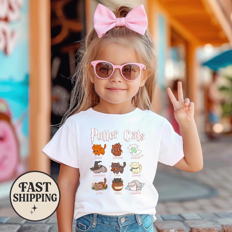 May include: White t-shirt with the text "Potter Cats" and illustrations of cats in various poses. The shirt is worn by a young girl wearing pink sunglasses and a pink bow. The girl is giving a peace sign.