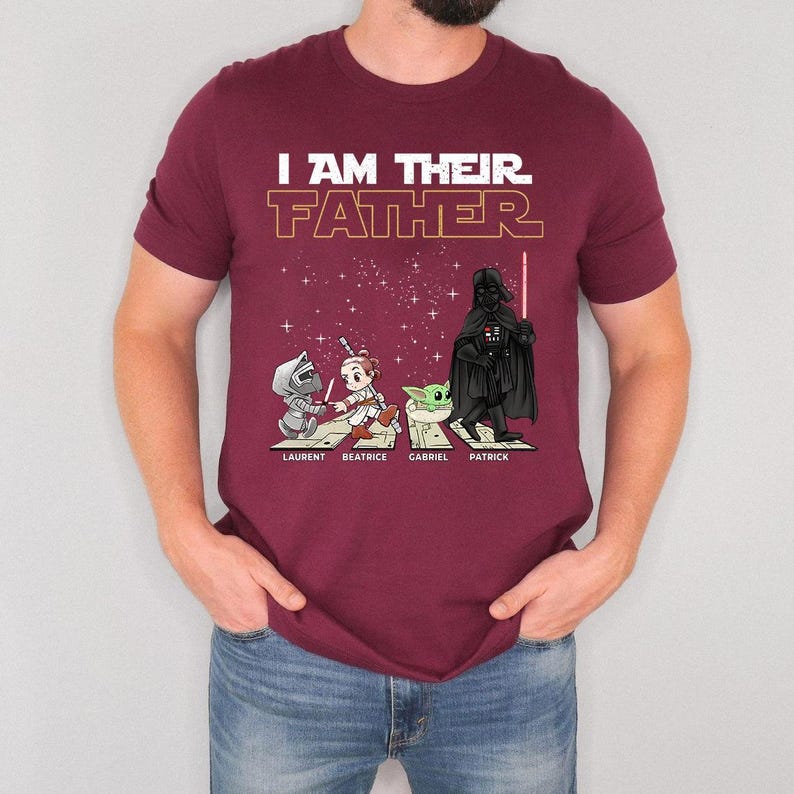 May include: Burgundy t-shirt with the text "I AM THEIR FATHER" in white and gold. Below the text are illustrations of characters from a popular science fiction franchise. The names "LAURENT", "BEATRICE", "GABRIEL", and "PATRICK" are printed below the characters.