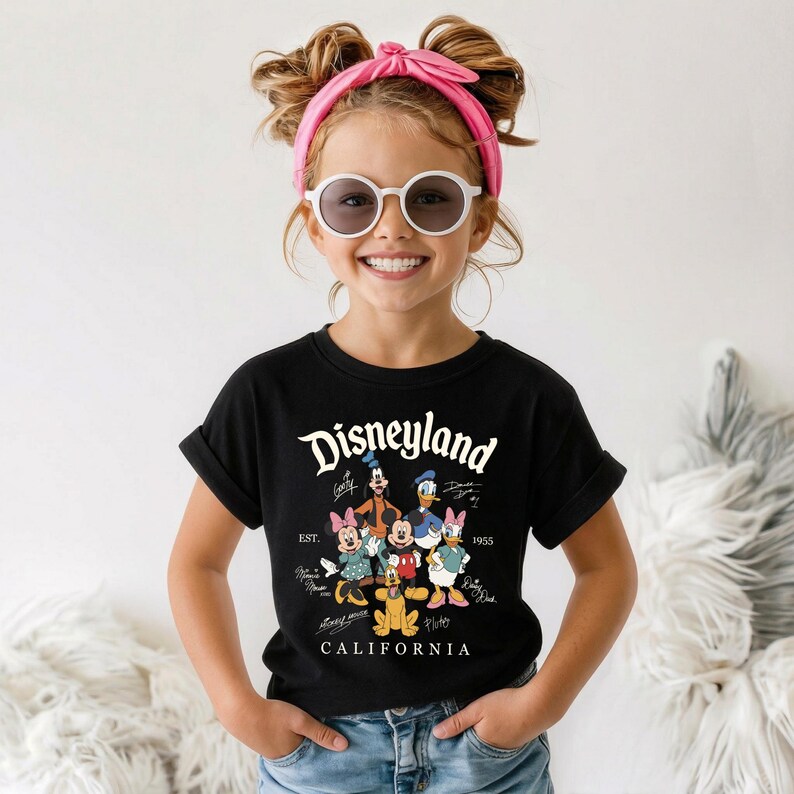 May include: Black t-shirt featuring the Disneyland logo and various Disney characters, including Mickey Mouse, Minnie Mouse, and Donald Duck. The shirt also includes the text "CALIFORNIA" and the year "1955".