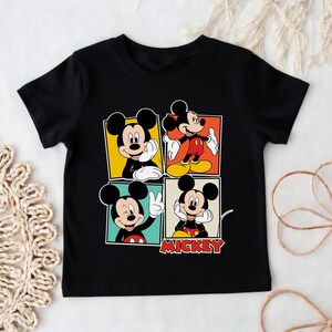 May include: Black t-shirt with a colourful graphic of Mickey Mouse in four different poses. Each Mickey is in a different coloured square, with the word "Mickey" in red below. A fun, cartoon-style design.