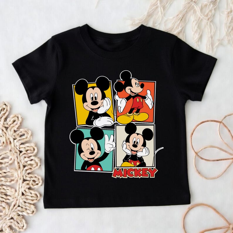 May include: Black t-shirt with a colourful graphic of Mickey Mouse in four different poses. Each Mickey is in a different coloured square, with the word "Mickey" in red below. A fun, cartoon-style design.