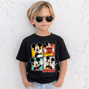 May include: Black t-shirt with four panels displaying Mickey Mouse images. The panels have yellow, orange, green, and blue backgrounds. The word "Mickey" is printed in red at the bottom of the shirt.