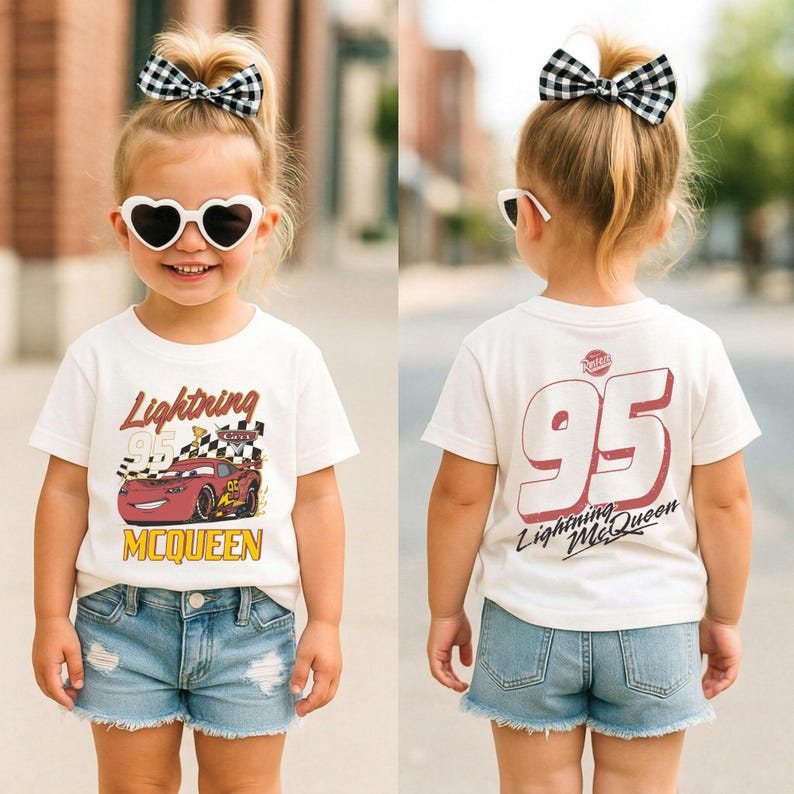May include: A child wearing a white t-shirt with a Lightning McQueen graphic and the number 95. The shirt is paired with denim shorts and a black and white checkered bow. The child is also wearing heart-shaped sunglasses.