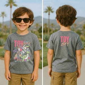 May include: A gray t-shirt featuring the text "TOY STORY" with a graphic of characters from the movie. The shirt has a crew neck and short sleeves. The back of the shirt also has the text "TOY STORY".