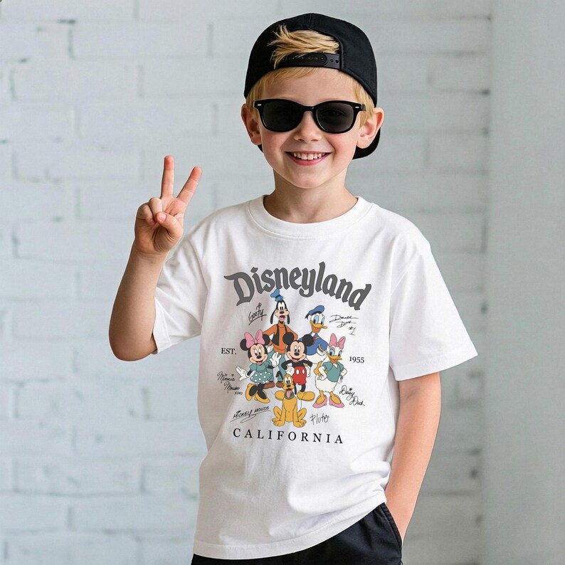 May include: A white t-shirt featuring a Disneyland graphic with Mickey Mouse, Minnie Mouse, Donald Duck, Daisy Duck, Goofy, and Pluto. The shirt has the text "Disneyland California" and "EST. 1955". The person is wearing a black cap and sunglasses.