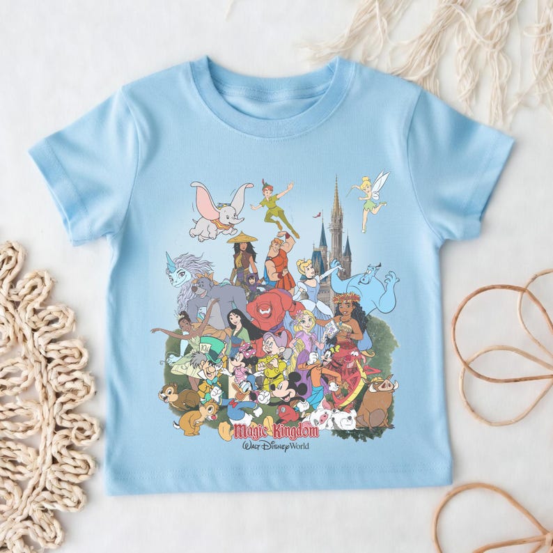 May include: Light blue t-shirt featuring a colorful graphic of various Disney characters, including Dumbo, Peter Pan, and Mickey Mouse. The text "Magic Kingdom, Walt Disney World" is printed at the bottom of the graphic. The shirt is made of a soft material.
