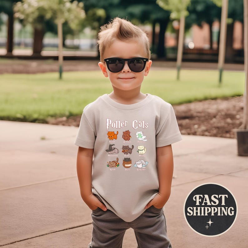 May include: A young child wearing a light gray t-shirt with the words "Potter Cats" printed on the front. The shirt features cartoon cat illustrations. The child is wearing sunglasses and gray pants.