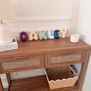 May include: A set of individual, rounded, three-dimensional letters spelling the name OAKLEY in various colours including dark red, light yellow, sage green, light blue, dark blue, and peach, displayed on a wooden console table.
