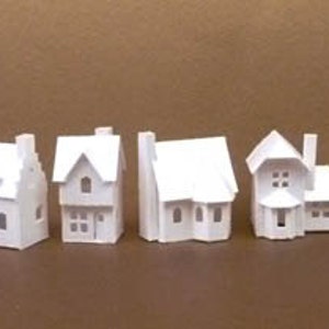 May include: A set of ten white paper model houses, each with unique architectural details. The houses are arranged in a row on a brown surface.