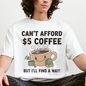 May include: White t-shirt with the text "CAN'T AFFORD $5 COFFEE" above a smiling coffee cup graphic. Below the graphic is the text "BUT I'LL FIND A WAY!". The shirt also features a wallet and backpack graphic.