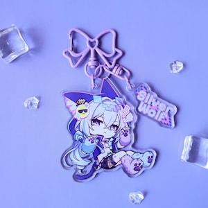 Puede incluir: Llavero acrílico transparente con un personaje de dibujos animados con orejas de gato, pelo azul y blanco y un atuendo negro. El llavero tiene una parte superior en forma de lazo y una etiqueta que dice "Silver Wolf". El fondo es morado claro.