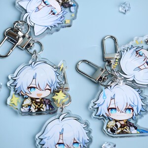 May include: Several clear acrylic keychains featuring a cartoon character with light blue hair and blue eyes. Each keychain has a silver clasp and a small charm. The character is depicted in various poses, some with a winking expression.