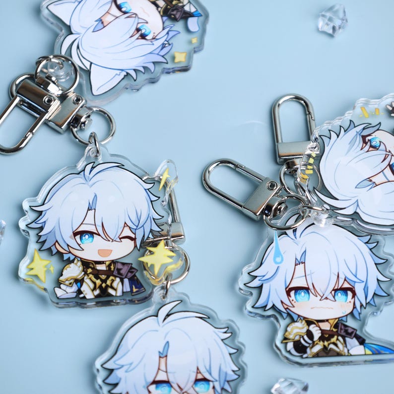 May include: Several clear acrylic keychains featuring a cartoon character with light blue hair and blue eyes. Each keychain has a silver clasp and a small charm. The character is depicted in various poses, some with a winking expression.