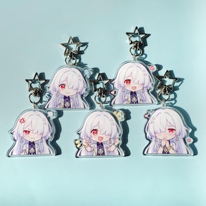 Puede incluir: Conjunto de seis llaveros de estilo anime. Cada llavero presenta un personaje con cabello blanco y ojos rojos. Cada uno tiene un dije en forma de estrella y un anillo plateado. Las expresiones del personaje varían.