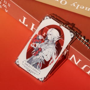 May include: A clear acrylic keychain featuring a character illustration. The design includes a character with white hair, holding red flowers, and the name "Arlecchino". The keychain has a silver ball chain.