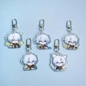 May include: Five acrylic keychains featuring a cartoon character with white hair and blue eyes. Each keychain has a silver clasp. The character is depicted in various poses, some with star or cat-shaped accents. The background is a light blue.