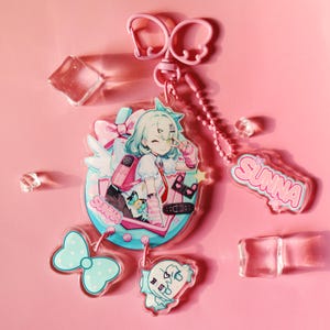 Pode incluir: Um conjunto de pingentes e chaveiros de acrílico com uma menina de desenho animado com cabelo turquesa, uma mochila rosa e a palavra "SUNNA". Os pingentes incluem um laço, uma figura fantasmagórica e um fecho de chaveiro rosa. O fundo é rosa.