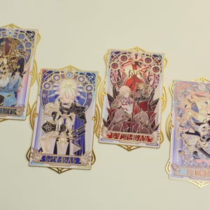 Puede incluir: Varios pines decorativos rectangulares con diseños intrincados. Cada pin presenta una ilustración de personaje al estilo vidriera, con marcos dorados. La paleta de colores incluye azules, rojos y dorados, creando una apariencia detallada y artística.