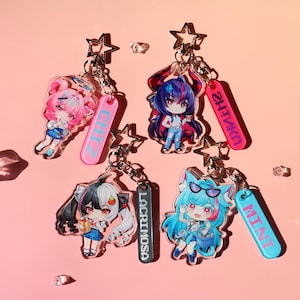 Puede incluir: Cuatro llaveros de acrílico con personajes de anime estilo chibi y cierres en forma de estrella. Cada dije incluye una etiqueta rectangular con texto: CHIZ en azul sobre rosa, SHINKA en morado sobre rosa, LACRIMOSA en blanco sobre negro y MINT en rosa sobre azul.