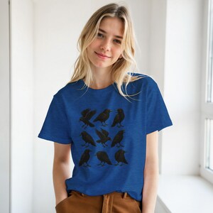 May include: A royal blue t-shirt with a pattern of nine black crows in different poses. The crows are illustrated with detailed wings and beaks. The shirt is made of a soft material.