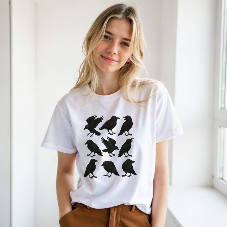 May include: White t-shirt with a grid of nine black raven illustrations. The ravens are shown in different poses, some with wings open, others perched. The shirt is made of a soft material, suitable for casual wear.