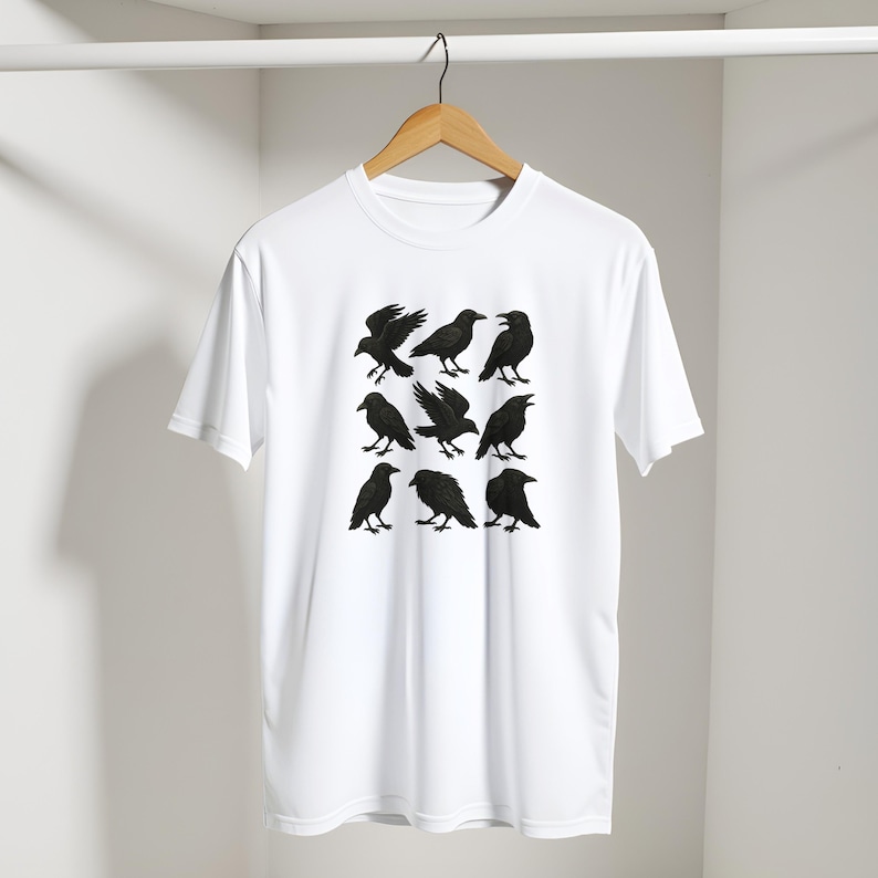 May include: White t-shirt with a design of nine black crows in different positions. The crows are rendered as detailed silhouettes, contrasting sharply against the white material. The shirt is displayed on a wooden hanger.