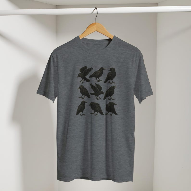 May include: A grey t-shirt displaying a grid of nine black raven illustrations. The ravens are shown in different poses, some with wings extended, others perched. The design is centrally placed on the shirt.