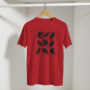 May include: A red t-shirt with a design of nine black raven illustrations arranged in a grid. The ravens are shown in different poses. The t-shirt is hanging on a wooden hanger.