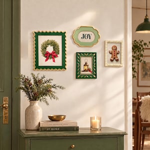 Può includere: Una decorazione da parete con quattro stampe incorniciate: una cornice verde smerlata con una ghirlanda, una cornice verde chiaro con la scritta JOY, una cornice verde scuro con una lanterna e una cornice color crema con perline e un omino di pan di zenzero.