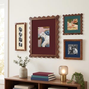 May include: A gallery wall arrangement featuring four wooden picture frames with scalloped or beaded edges. The frames contain various photographs, including a white cat on a blue chair, a person with a dog, and a vertical strip of portraits.