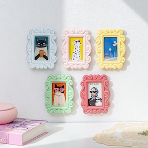 May include: Five decorative picture frames in pastel shades of blue, pink, yellow, green, and coral. Each frame contains a different illustration, including a cat, a Dalmatian, and a woman. The text "be cool" is visible on one of the frames.