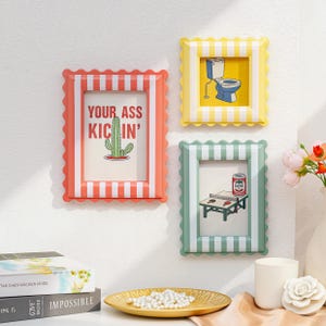 May include: Three decorative picture frames with scalloped edges and striped borders. The frames are in coral, yellow, and green. Each frame contains a different image: a cactus, a toilet, and a ping pong table. The coral frame reads "YOUR ASS KICKIN'."