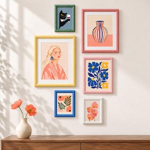 Könnte beinhalten: Eine Galerie-Wand mit sechs gerahmten Kunstdrucken in grünen, rosa, gelben und blauen Perlenrahmen. Die Motive zeigen eine schwarze Katze mit Weinglas, eine gestreifte Vase, ein Porträt einer Person sowie verschiedene florale Illustrationen.