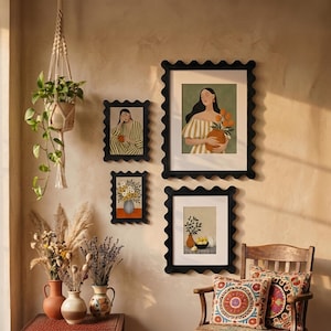 May include: A wall display featuring three black scalloped frames containing illustrations of a person with flowers, a floral arrangement, and a still life. A macrame plant hanger with a green plant and three ceramic vases with dried flowers.