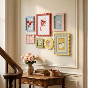 May include: A gallery wall arrangement featuring seven wavy-edged picture frames in red, blue, pink, green, and yellow. The frames contain various illustrations including tomatoes, a person, a chair, flowers, a teacup, and a white bag.