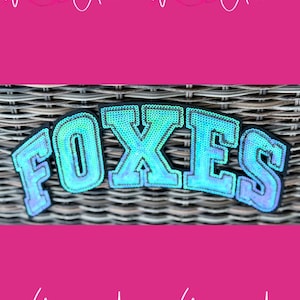 May include: A teal sequined patch with the word "FOXES" in large, stylized letters. The patch is outlined in black and sits against a woven background. The image has a pink border with the text "With Andi" repeated.