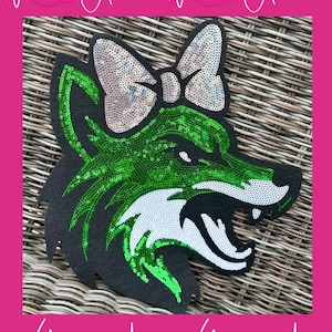 May include: A black sequined wolf head patch with a green and silver bow. The wolf's face is detailed with green sequins, white teeth, and a silver bow. The text "With Andi" is written in white script.