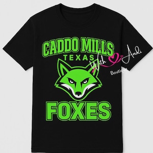 May include: Black t-shirt with a green fox head graphic and the words "CADDO MILLS TEXAS FOXES" in green. The shirt also has the text "With Andi Boutique" in white and pink.