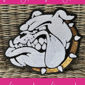 May include: A sequined bulldog patch in black, white, and gold. The bulldog's head is the focal point, with white sequins forming the face and black outlining the features. Gold sequins border the patch. The text "With Andi" is repeated.