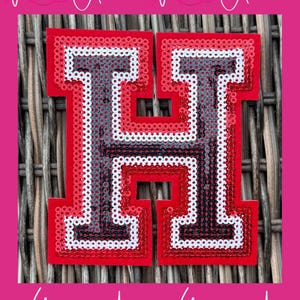 May include: A red, white, and gray sequined letter "H" on a red background. The letter is outlined in red sequins, with white and gray sequins filling the interior. The background is a woven texture, with the words "With Andi" repeated.