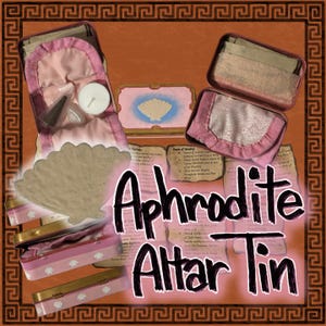 Op de afbeelding: Een Aphrodite Altaarblik met roze en gouden accenten. Het blik bevat diverse items, waaronder een schelp, kaarsen en kleine containers. De tekst "Aphrodite Altar Tin" is prominent aanwezig.