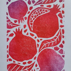 May include: A linocut print in red and purple depicting pomegranates and leaves. The pomegranates are shown at different stages of ripeness. The background is white with a mosaic pattern.