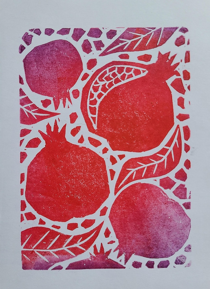May include: A linocut print in red and purple depicting pomegranates and leaves. The pomegranates are shown at different stages of ripeness. The background is white with a mosaic pattern.