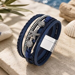 Può includere: Un bracciale blu navy a più fili con cordini in pelle intrecciata, una fila di piccole perline color argento e tre ciondoli in metallo color argento a forma di stella marina e due conchiglie, fissato con una chiusura magnetica rettangolare.