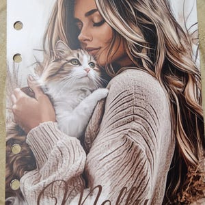 Könnte beinhalten: Ein Druck, der eine Frau mit langen blonden Haaren zeigt, die zärtlich eine flauschige Katze umarmt. Die Katze hat weißes und braunes Fell. Das Wort "Molly" ist in Schreibschrift geschrieben. Der Druck enthält auch den Text "Flower Boutique By Manu" und "Artbr 340".