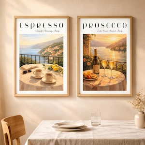 May include: Two framed prints, one labeled "Espresso Amalfi Morning, Italy" and the other "Prosecco Lake Como Sunset, Italy." Each depicts a scenic Italian landscape with a table set for drinks, including coffee and wine, respectively. The prints are in wooden frames.