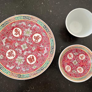 May include: Three red and white porcelain plates with Chinese characters. The largest plate has a red and white floral design with a gold border. The two smaller plates have a similar design but are smaller in size.