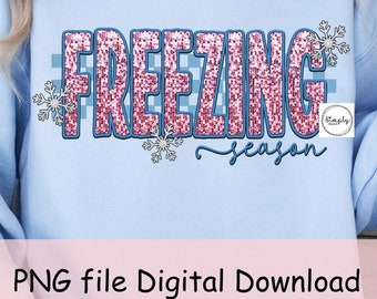 May include: A light blue sweatshirt with the text "Freezing Season" in pink glitter letters with a blue and white checkered background. There are snowflakes and a small logo that says "Simply Designed" on the sweatshirt.