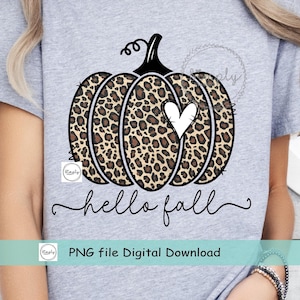 May include: A gray t-shirt with a black and brown leopard print pumpkin with a white heart in the center. The text "hello fall" is written in black cursive below the pumpkin. The text "PNG file Digital Download" is written in black below the text "hello fall".