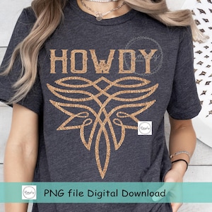 May include: A dark gray t-shirt with a gold graphic design that says "HOWDY" and features a stylized floral pattern. The design is centered on the shirt.